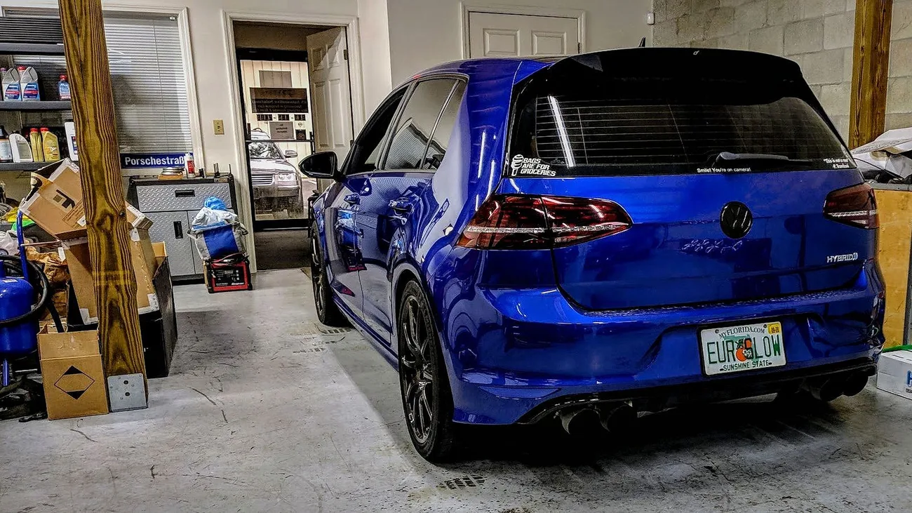 A blue Volkswagen Golf R inside the workshop next to a Porschestrasse sign